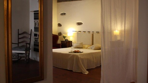 A bedroom with a bed, bedside table, lamp, and a mirror. - Il Lupo Rosso (Santu Lussurgiu)