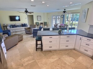 A spacious kitchen with a large island, a dining area with chairs, a sofa, and a TV mounted on the wall. - Relax, recharge, and indulge—enjoy waterfront views, spa, pool, and offers (Cape Coral)