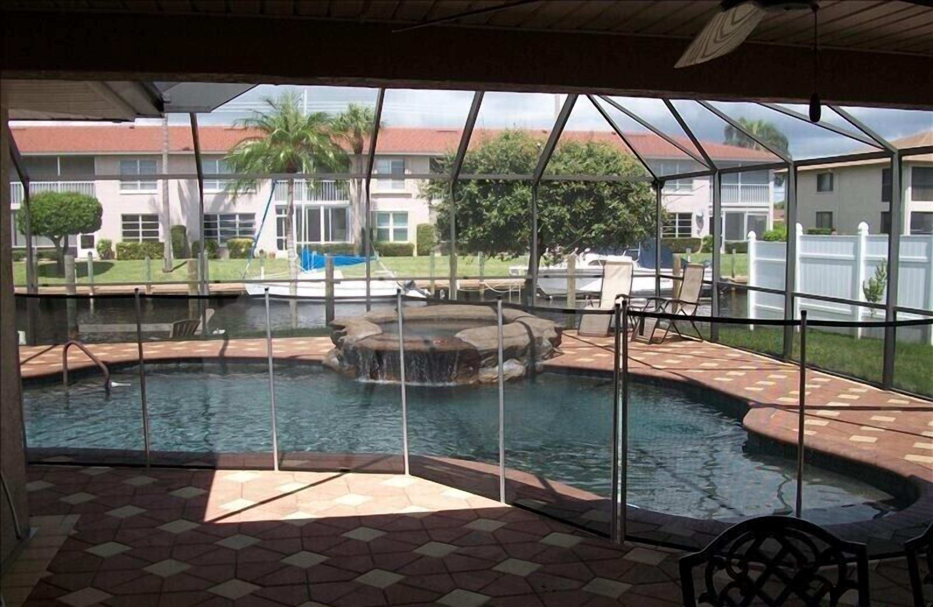 Piscina exterior cubierta con fuente, rodeada por una terraza con sillas y vistas a edificios residenciales.