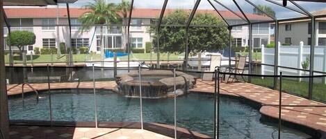 Piscina exterior cubierta con fuente, rodeada por una terraza con sillas y vistas a edificios residenciales.