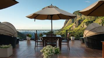 Una terraza con mesa y sillas, rodeada de sombrillas grandes, con vistas a un paisaje montañoso.