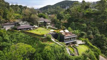 A modern house with a well-maintained garden, surrounded by lush greenery and hills.