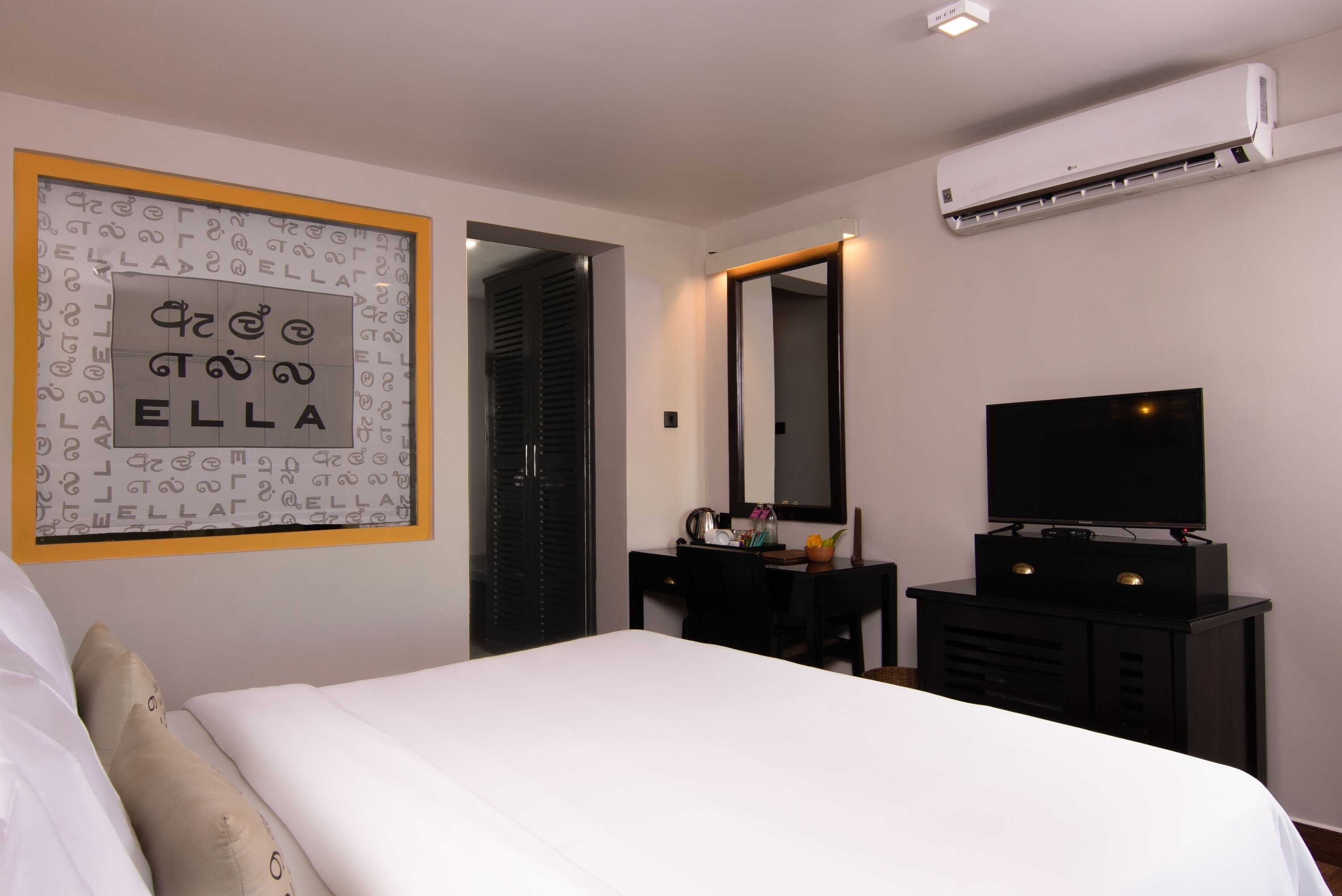 Ein Hotelzimmer mit Bett, Schreibtisch mit Spiegel, Flachbildfernseher und Klimaanlage.