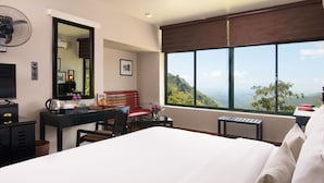 A hotel room with a bed, a desk with a chair, a small table with a keyboard, a red bench, a fan, a large window with a view of the mountains, and a mirror on the wall. - EKHO Ella (Ella)