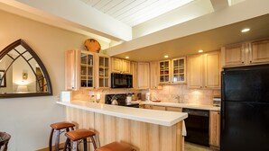 A modern kitchen with wooden cabinets, a black refrigerator, and a bar area with stools. - CA111 | Pool | Slopeside w/ Great Views | Winter Shuttle | Hot Tub (Steamboat Springs)