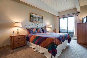 Een slaapkamer met een bed, twee nachtkastjes, een raam met gordijnen, een schilderij aan de muur en uitzicht op het exterieur.