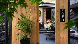 Una entrada de madera con un letrero que dice "EAST 3", que da a un espacio al aire libre con una mesa y sillas.