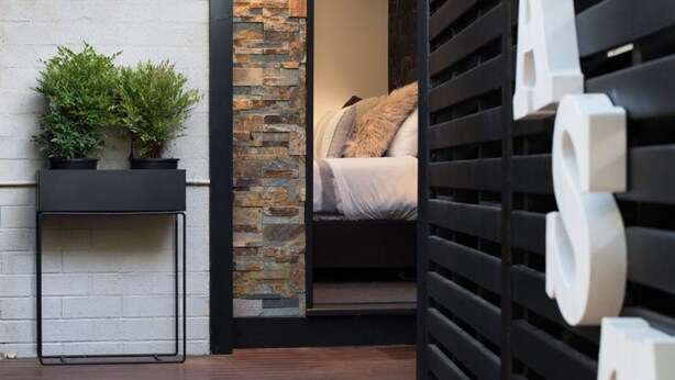 Una habitación moderna con una cama, una mesita con una planta y una pared de ladrillo.