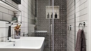 Un baño moderno con lavamanos blanco, cabina de ducha con mampara de vidrio y azulejos estampados.