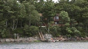 A river with a boat docked near a forested area with a building in the background. - Three month rental minimum.   (Greenland)