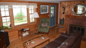 A cozy living room with wooden walls, a green armchair, a brown leather sofa, a coffee table, and a fireplace. - Three month rental minimum.   (Greenland)