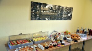 A buffet table with various food items and beverages, a painting on the wall, and a wooden floor. - Villa Rosamunde (Burg (Spreewald))