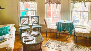 A cozy room with a sofa, two chairs, a small table, and a laptop. There are three windows with star-patterned curtains. - Pet Friendly-Steps from All-Harbor View Apt Heart of Boothbay Harbor's Downtown. (Boothbay Harbor)