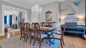 Une salle à manger avec une table ronde, des chaises en bois, un lustre, un piano et un miroir au mur.