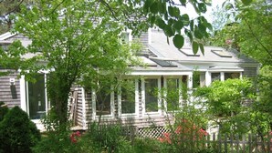 A house with a covered porch, surrounded by lush greenery and a wooden fence. - Eastham home near the water & bike path; large screened in porch - Pet Friendly (Eastham)