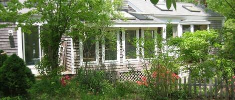 A house with a covered porch, surrounded by lush greenery and a wooden fence.