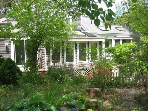 A house with a covered porch, surrounded by lush greenery and a wooden fence. - Eastham home near the water & bike path; large screened in porch - Pet Friendly (Eastham)