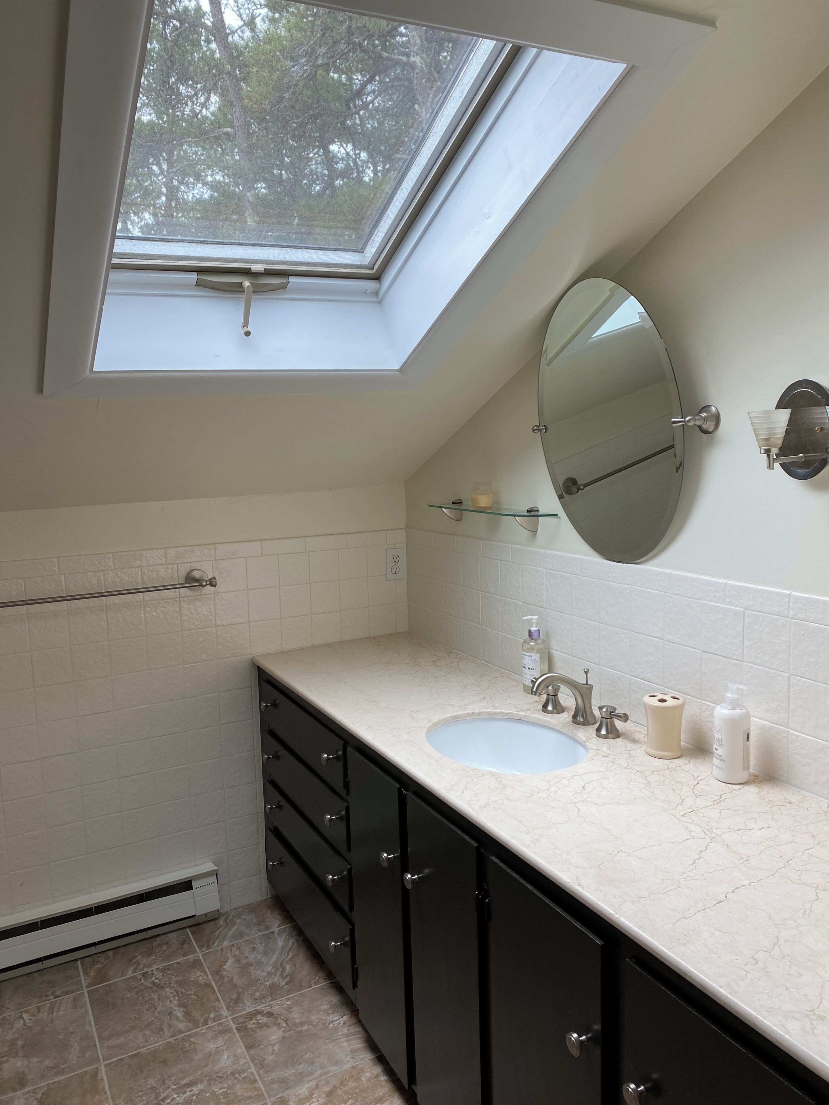 A bathroom with a skylight, a large mirror, a sink, and a towel rack.