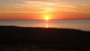 A sunset over a calm sea with a beach in the foreground. - Eastham home near the water & bike path; large screened in porch - Pet Friendly (Eastham)