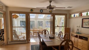 A spacious dining area with a wooden table and chairs, large windows, and a ceiling fan. - Eastham home near the water & bike path; large screened in porch - Pet Friendly (Eastham)