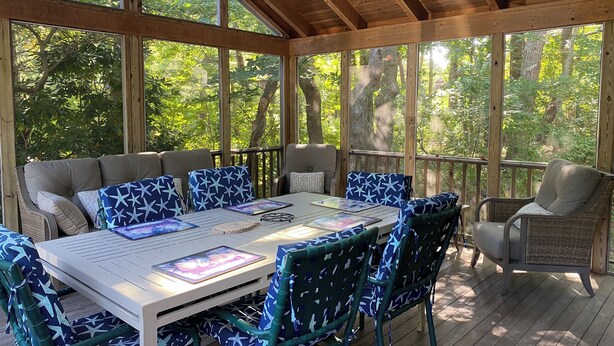 A covered outdoor seating area with a table and chairs, surrounded by large windows offering views of trees. - Eastham home near the water & bike path; large screened in porch - Pet Friendly (Eastham)