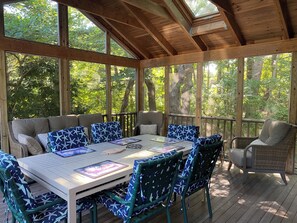 A covered outdoor seating area with a table and chairs, surrounded by large windows offering views of trees. - Eastham home near the water & bike path; large screened in porch - Pet Friendly (Eastham)