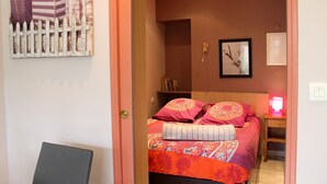 A bedroom with a bed, a nightstand, a lamp, a framed picture on the wall, and a door leading to another room. - Studio Cap d'Erquy - Villas des Sables (Fréhel)