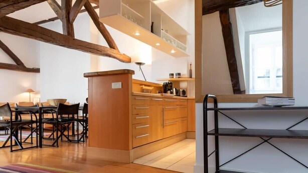 Une cuisine moderne avec des meubles en bois, un coin repas avec des chaises et une étagère en métal noir.