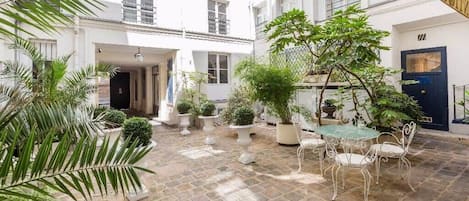 Une cour avec une table et des chaises, entourée de plantes en pot et dotée d’un sol en pierre.