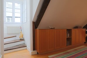 A room with wooden flooring, a staircase with a radiator, a wooden cabinet, and a colorful striped rug.