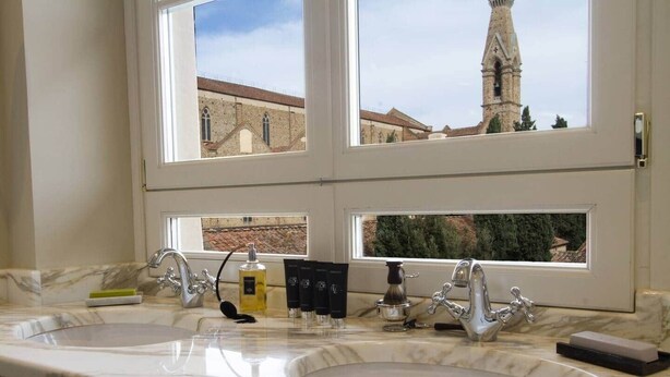 A bathroom with two sinks, a window with a view of a church and tower, and toiletries on the counter. - Luxury Suite Apartment of 200sqm with terrace (Firenze)