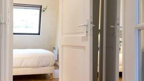 A bedroom with a bed, a window, and a sliding door leading to another room. - Coquelicot | Delightful 1 Bedroom Apt near Eiffel Tower (Paris)