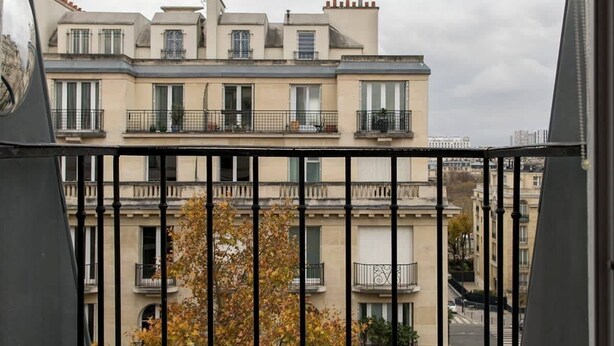 A balcony with a metal railing overlooking a row of buildings with multiple stories and balconies. - Coquelicot | Delightful 1 Bedroom Apt near Eiffel Tower (Paris)