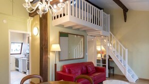 A dining area with a wooden table and chairs, a red leather sofa, a white round table, and a staircase leading to an upper level. - Coquelicot | Delightful 1 Bedroom Apt near Eiffel Tower (Paris)