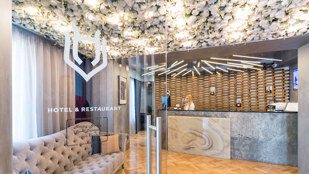 A hotel reception area with a plush sofa, a reception desk, and a wall decorated with white flowers. - Venis Boutique Hotel (Bucharest)