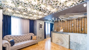 A reception area with a plush sofa, a marble reception desk, and a ceiling adorned with white flowers. - Venis Boutique Hotel (Bucharest)