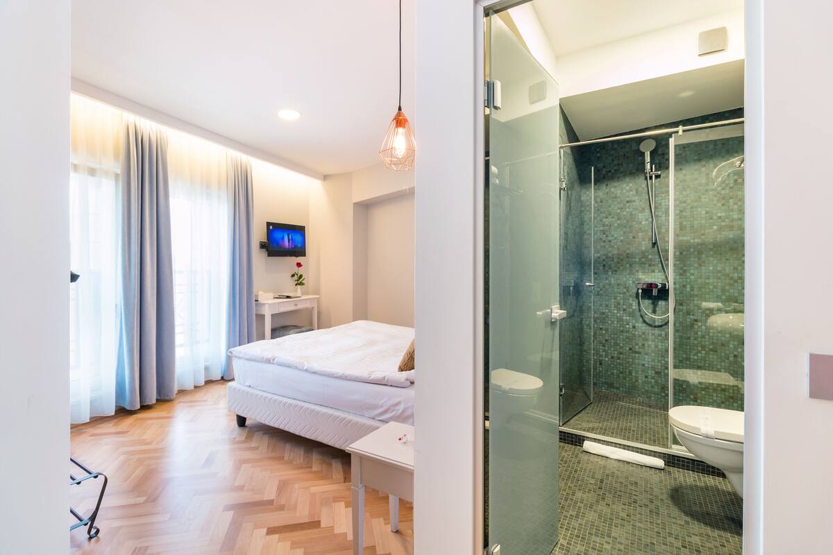 Una habitación de hotel moderna con cama, mesita de noche, televisión y zona de ducha con mampara de vidrio.
