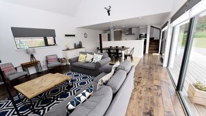 A spacious living area with a large gray sofa, a wooden coffee table, and a patterned rug. There is a kitchen in the background with a dining table and chairs. - Stunning 4 bedroom countryside retreat (Aberlour)