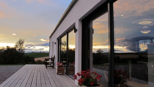 A modern building with large windows, a wooden deck, and outdoor seating. - Stunning 4 bedroom countryside retreat (Aberlour)