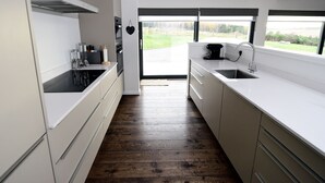 A modern kitchen with white cabinets, a wooden floor, and a view of a green landscape through a large window. - Stunning 4 bedroom countryside retreat (Aberlour)