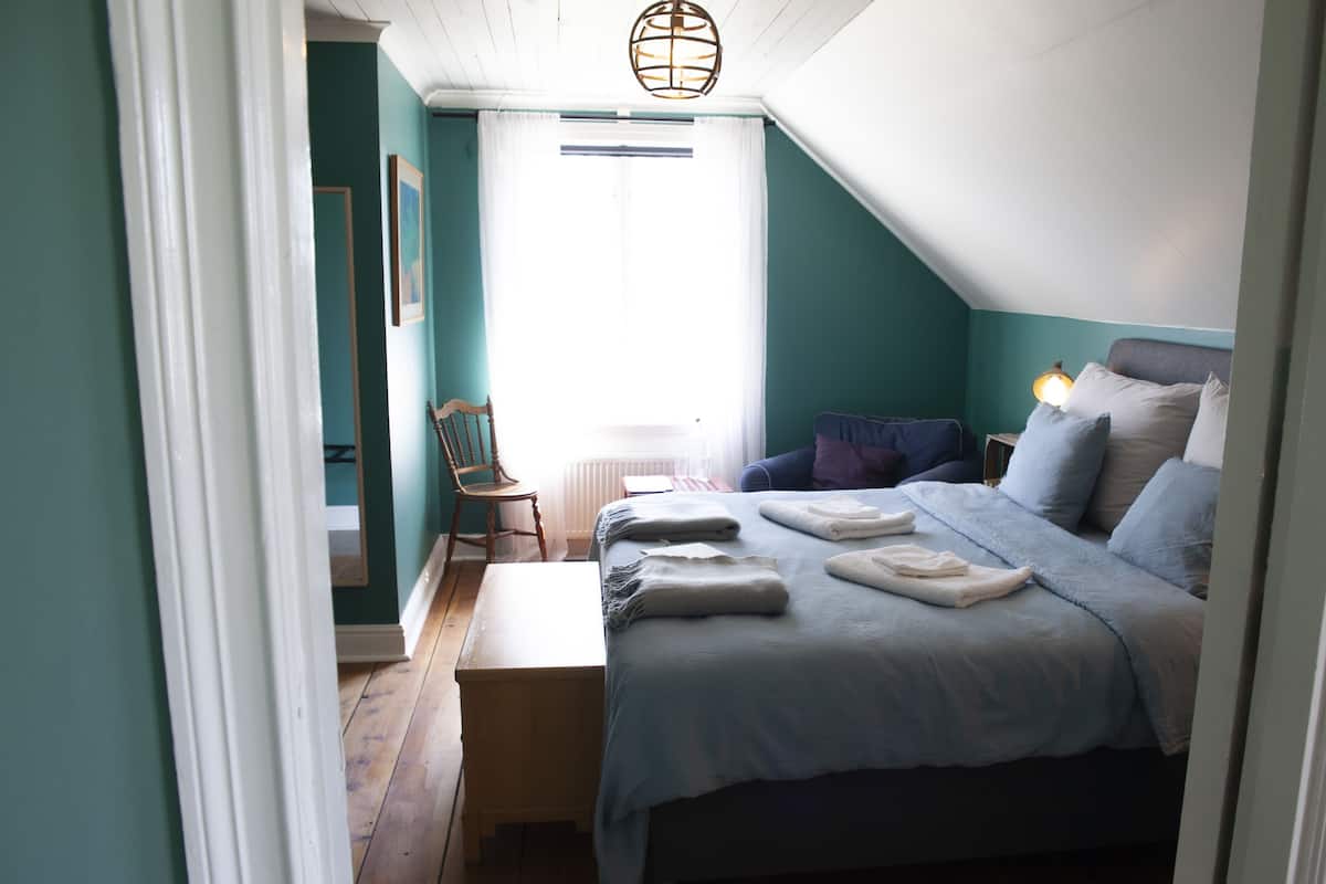 A bedroom with a bed, a bench, a chair, and a nightstand with a lamp.