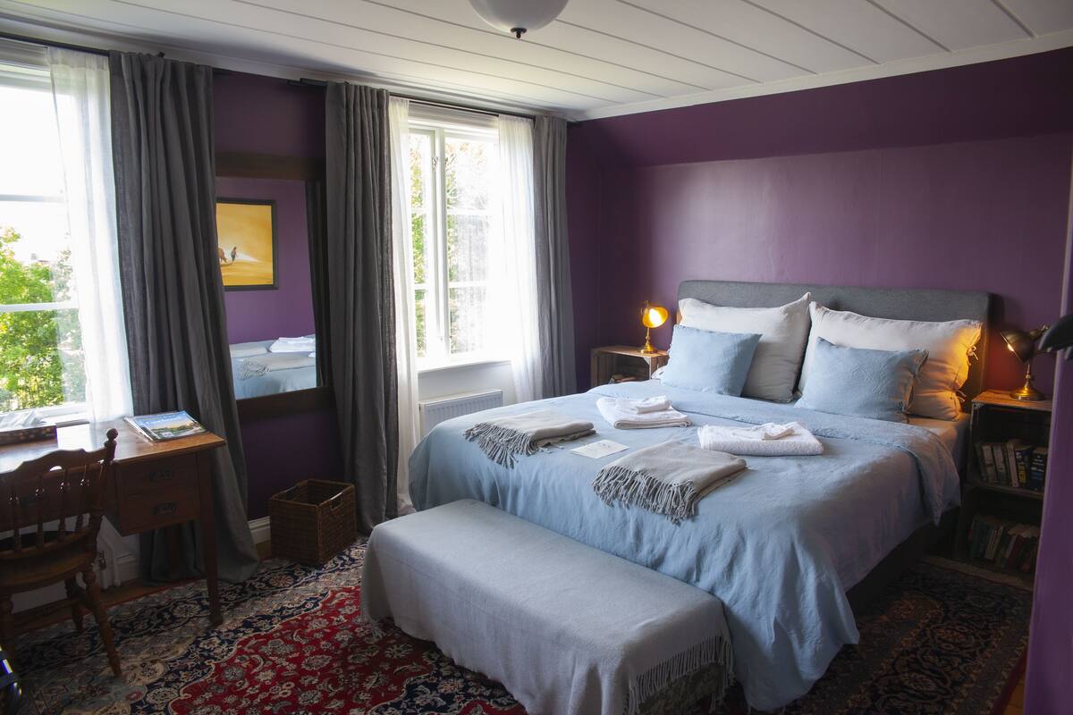 A bedroom with a bed, a desk, a chair, and a window with curtains.