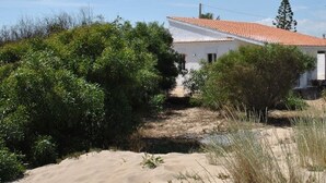 Ein weißes Gebäude mit rotem Ziegeldach, umgeben von üppiger Vegetation und Sanddünen.