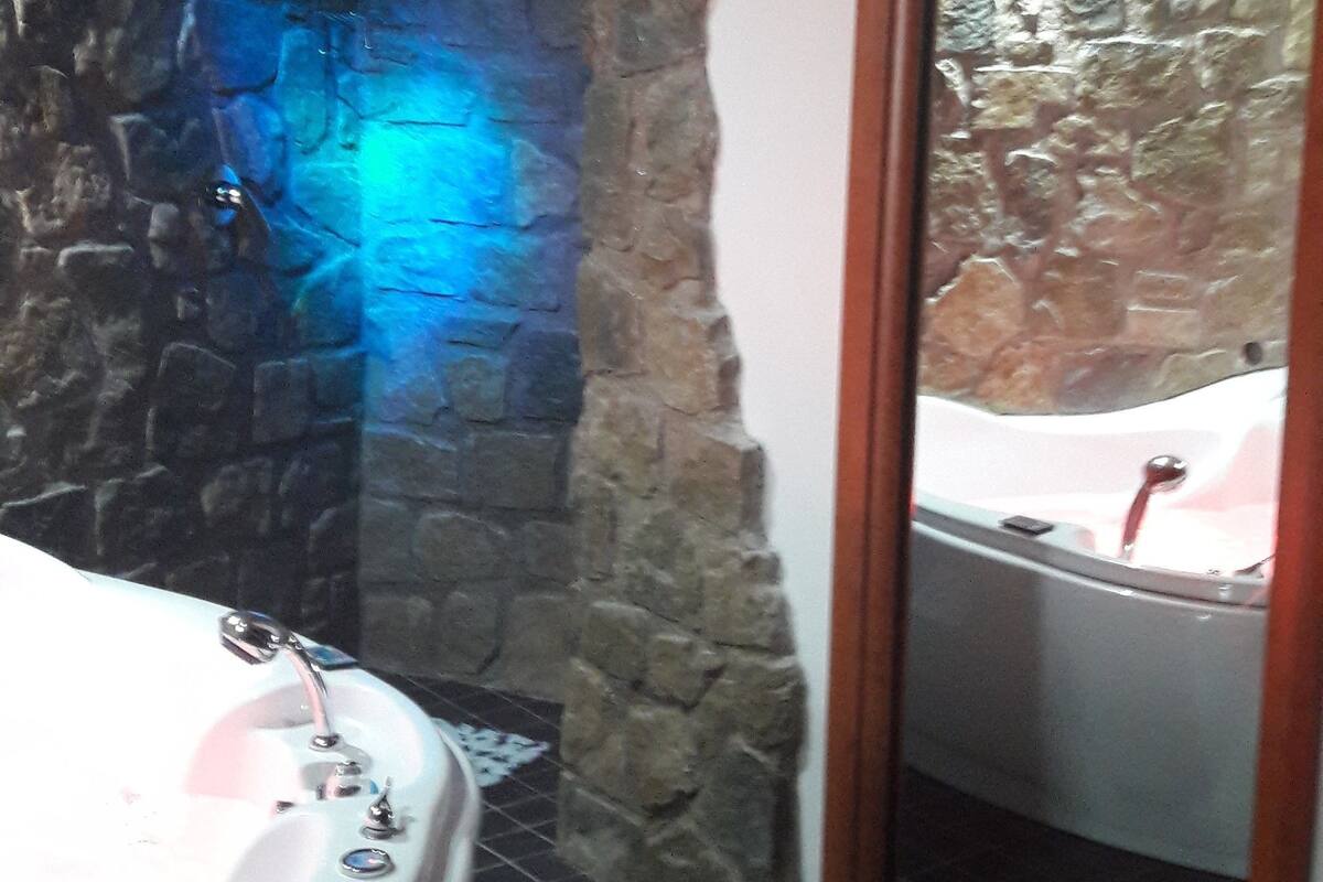 A bathroom with a stone wall, a bathtub, and a mirror reflecting a bathtub.