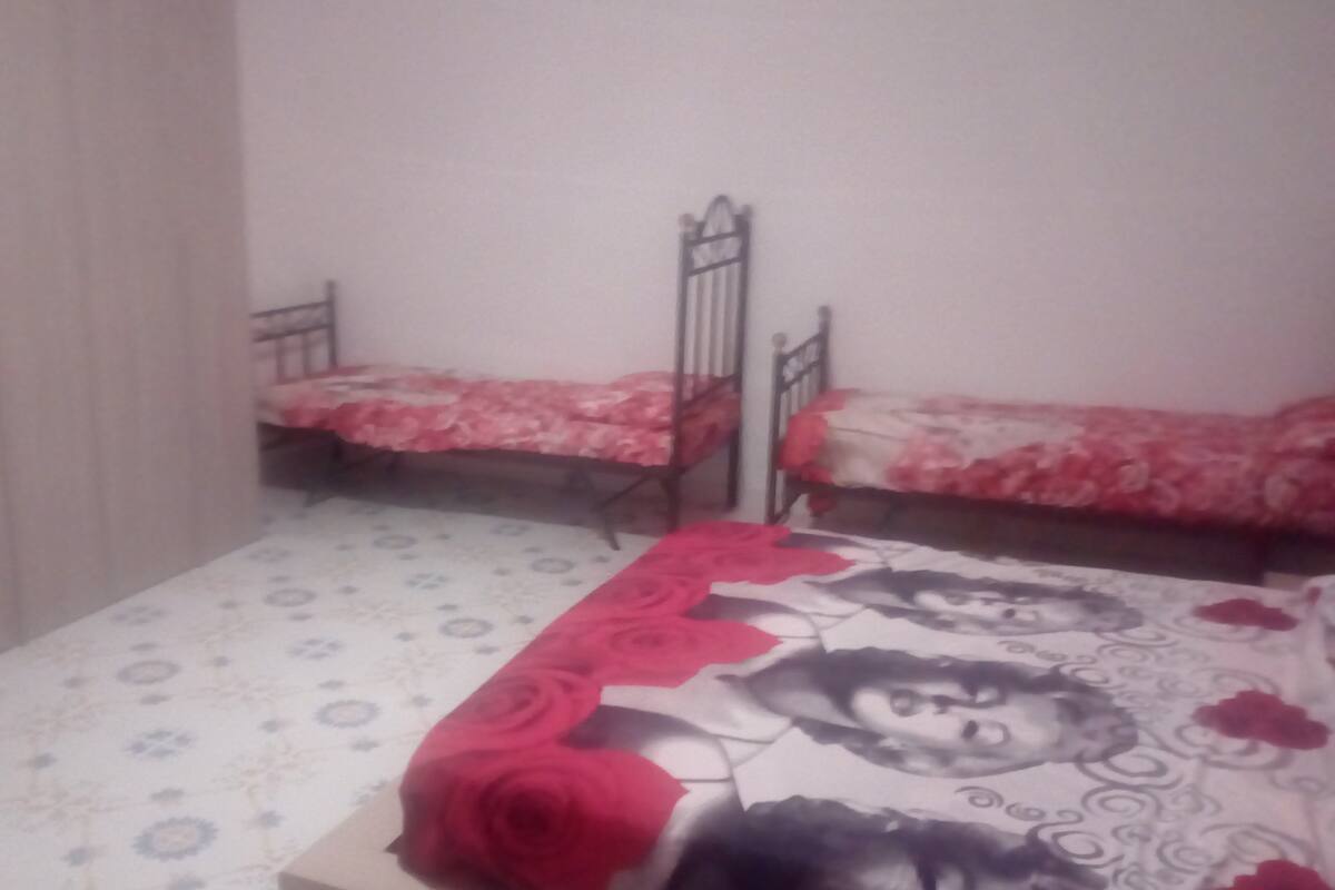 A bedroom with two single beds, each with a floral bedspread. The room has a patterned floor and a plain wall.