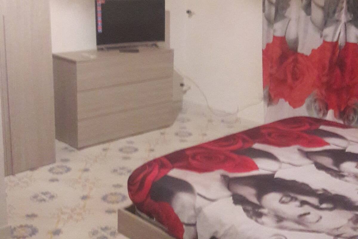 A bedroom with a bed, a dresser, a television on a stand, and a wall-mounted air conditioner.