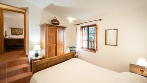 Une chambre à coucher avec un lit, une armoire en bois, une fenêtre avec des rideaux, une chaise et une lampe sur une table de chevet.