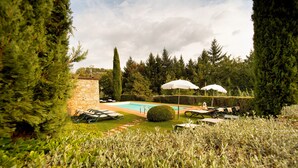 Un espace piscine agrémenté de chaises longues et de parasols, entouré de haies et d’arbres bien entretenus.