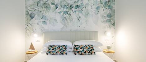 A bedroom with a large bed, two pillows with geometric patterns, a sailboat decoration, and a globe on a bedside table.