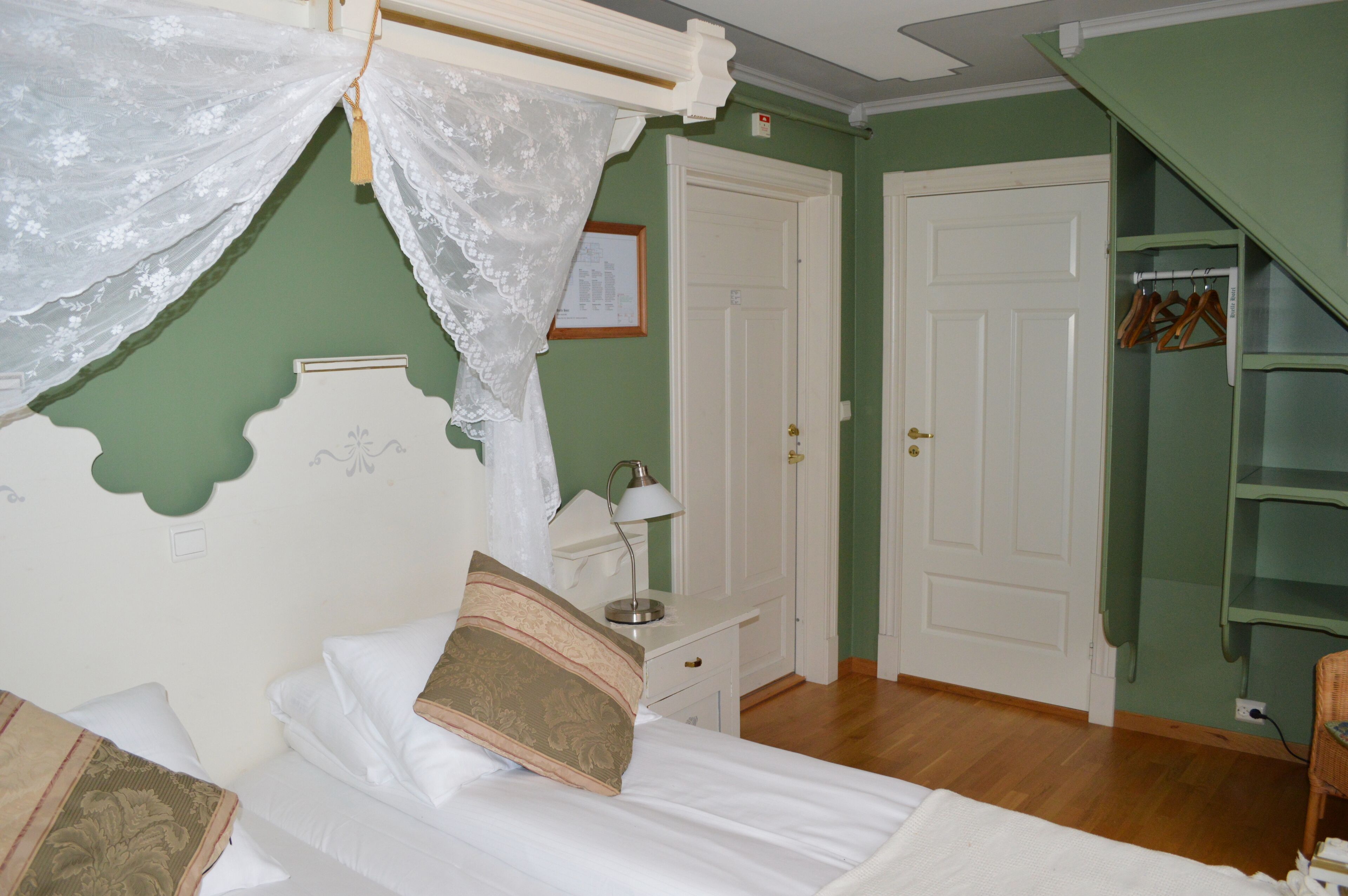 Een slaapkamer met een bed, nachtkastje, lamp, deur en een groene muur.
